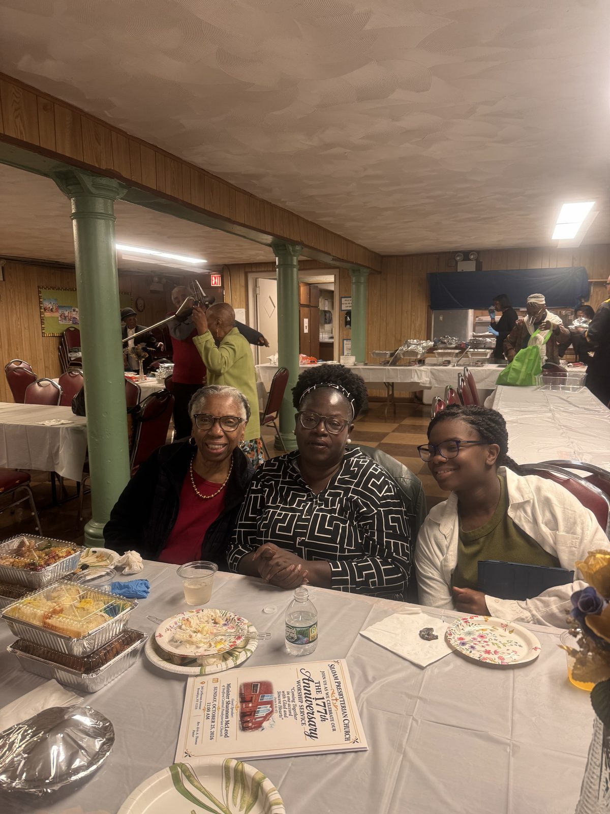 Three guests seated at a table in the fellowship hall, smiling